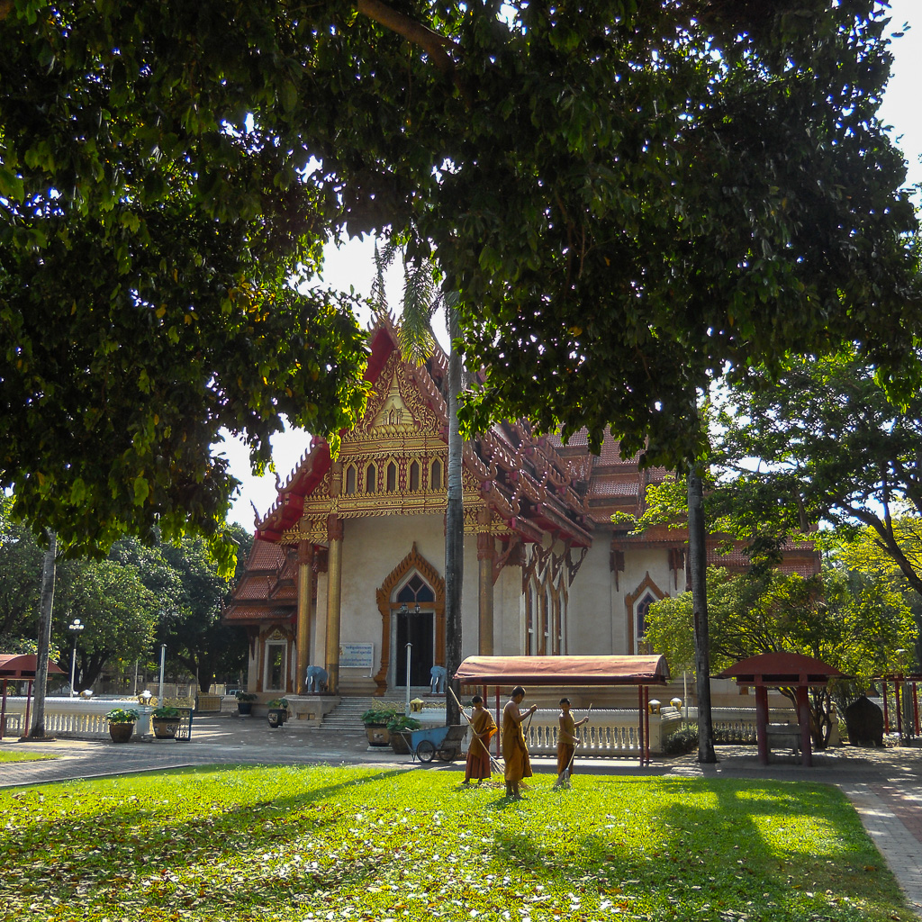 Monks sweeping leaves of the grass in front of the temple Wat Si Ubon Rattanaram.